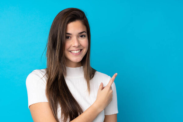 Девушка-подросток на изолированном синем фоне, указывая на сторону, чтобы представить продукт