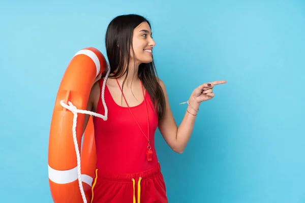 Lifeguard woman over isolated blue background with lifeguard equipment and pointing to the side to present a product