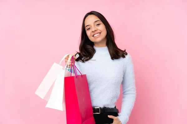 若いです女性とともにショッピングバッグ上の隔離されたピンクの背景笑い — ストック写真