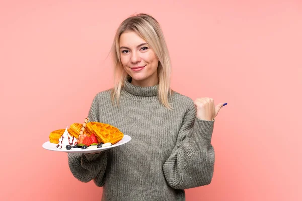 Jong Blond Vrouw Houden Wafels Geïsoleerde Roze Achtergrond Wijzend Naar — Stockfoto