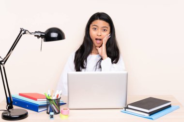İş yerindeki Asyalı öğrenci bilgisayarlı bir kız bej arka planda, şaşırmış ve şok olmuş bir yüz ifadesi ile izole edilmiş.