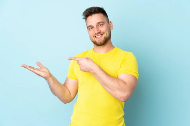 Mavi arka planda izole edilmiş Rus yakışıklı bir adam. Avucunun içinde hayali bir ilan tutuyor.