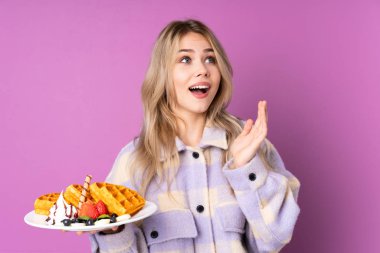 Mor arka planda yüzü sürpriz bir şekilde izole edilmiş waffle tutan Rus genç kız.