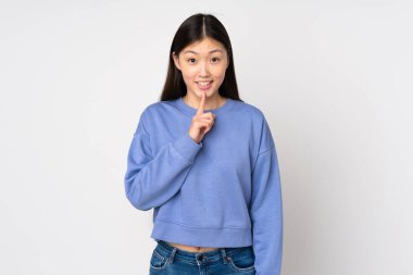 Arka planda izole edilmiş genç Asyalı bir kadın sessizlik işareti gösteriyor. Parmağını ağzına sokuyor.