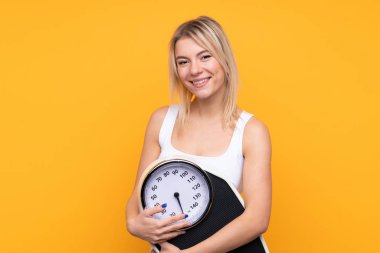 Genç sarışın Rus kadın, izole edilmiş sarı arka planda tartı makinesiyle.