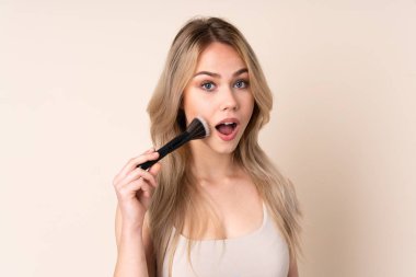 Makyaj fırçasıyla izole edilmiş arka planı olan genç sarışın kız.