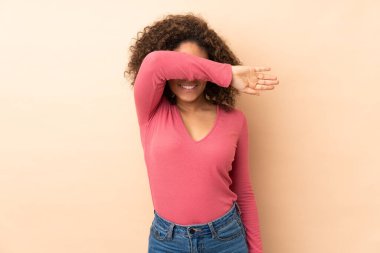 Genç Afrikalı Amerikalı kadın bej arka planda izole edilmiş, gözleri elle kapatılmış.