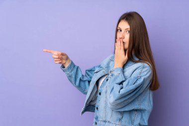 Mor arka planda izole edilmiş beyaz kız sürpriz bir ifadeyle bir yandan işaret ederken,