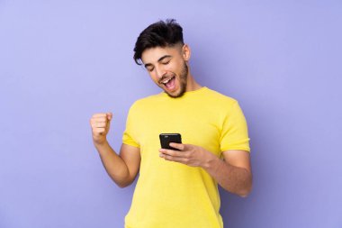 Arap yakışıklı adam izole edilmiş arka planda, telefon zafer pozisyonunda.