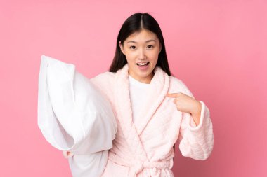 Pembe arka planda yüzü şaşırmış pijamalı genç bir Asyalı kadın.