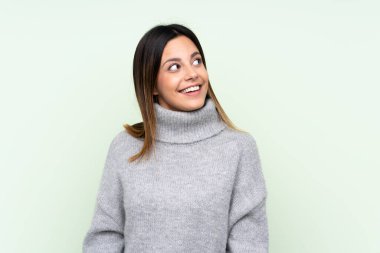 Yeşil arka planda kazak giyen bir kadın gülüyor ve yukarı bakıyor.