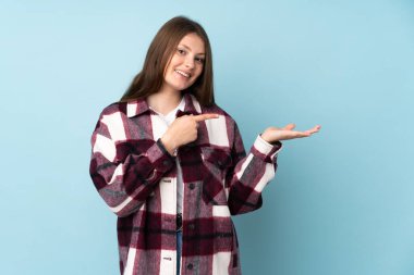 Mavi arka planda izole edilmiş genç beyaz kız, bir ilan vermek için avucunun içinde hayali bir fotokopi makinesi tutuyor.