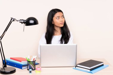 İş yerinde bej arka plan portresinden izole edilmiş dizüstü bilgisayarı olan Asyalı bir öğrenci.