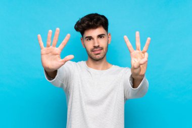 İzole edilmiş mavi arka plan üzerinde genç adam parmaklarıyla sekiz sayıyor.