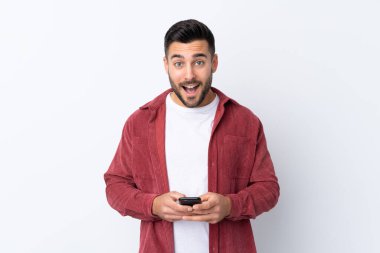 Sakallı, kadife ceket giyen genç yakışıklı adam izole edilmiş beyaz arka plan şaşırmış ve bir mesaj gönderiyor.