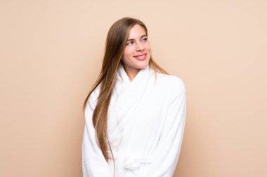 Bornozlu genç bir kız izole bir arka planda gülüyor ve yukarı bakıyor.