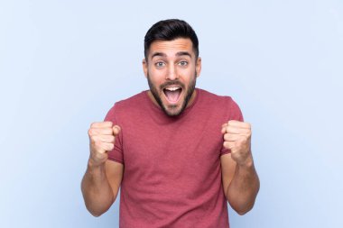 Mavi arka planda sakallı yakışıklı genç adam galibiyeti kutluyor.