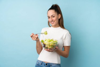 Genç esmer kadın mavi arka planda salata tutuyor.