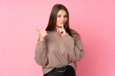 Pembe arka planda izole edilmiş genç beyaz bir kız. Yan tarafı işaret ediyor ve sessiz hareketler yapıyor.