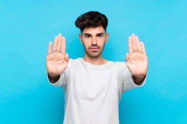 Soyutlanmış mavi arka planda genç bir adam dur hareketi yapıyor ve hayal kırıklığına uğruyor