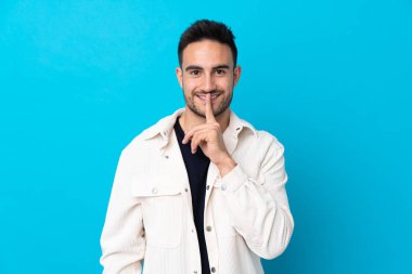 Soyutlanmış mavi arka planda genç yakışıklı adam sessizlik jesti yapıyor.