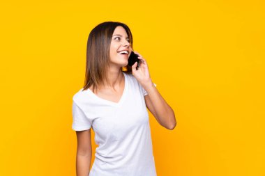 Cep telefonu ile bir konuşma tutmak izole sarı arka plan üzerinde genç kadın