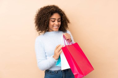 Genç Afrikalı Amerikalı kadın bej arka planda izole edilmiş. Elinde alışveriş torbaları var.