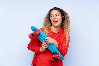 Mavi arka planda izole edilmiş kıvırcık saçlı, neşeli bir yüzü olan genç sarışın kadın.