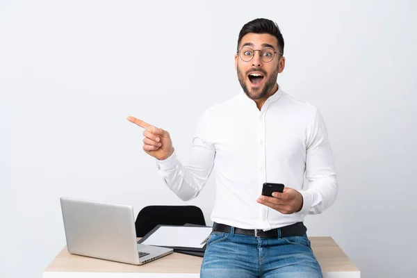 Jovem Empresário Segurando Telefone Celular Surpreso Apontando Dedo Para Lado — Fotografia de Stock