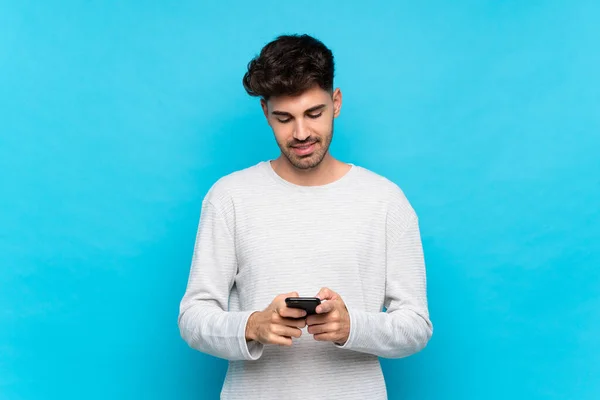 Joven Sobre Fondo Azul Aislado Enviando Mensaje Con Móvil —  Fotos de Stock