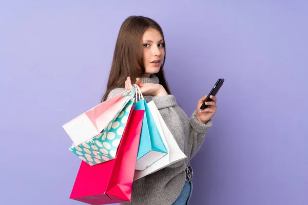 Nastolatek Biały Dziewczyna Odizolowany Fioletowy Tło Trzymając Zakupy Torby Telefon — Zdjęcie stockowe