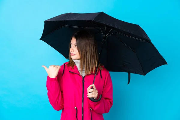 Mujer Joven Sosteniendo Paraguas Sobre Una Pared Azul Aislada Apuntando — Foto de Stock