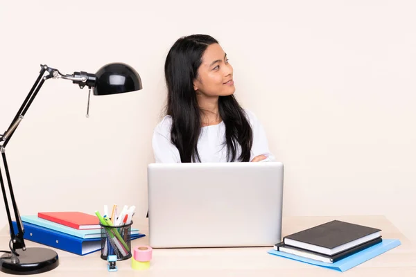 Student asian girl in a workplace with a laptop isolated on beige background in lateral position