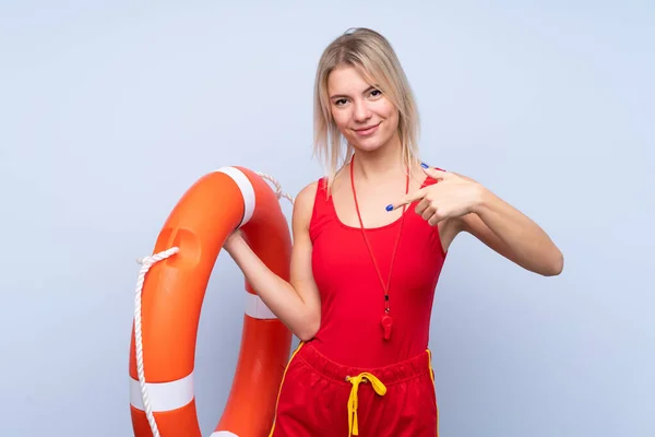 Lifeguard woman over isolated blue background with lifeguard equipment and pointing lifebuoy