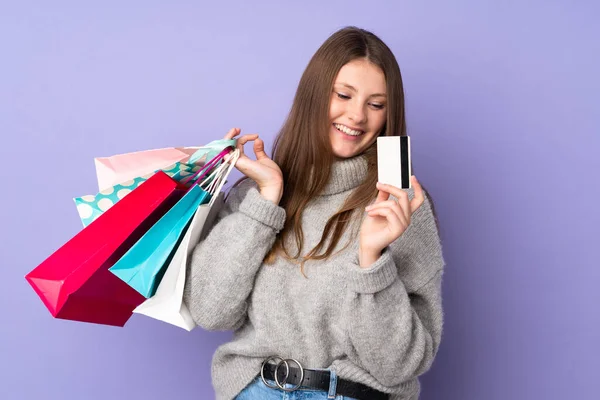 ティーネージャーCaucasian女の子孤立オンパープル背景保持ショッピングバッグとクレジットカード — ストック写真