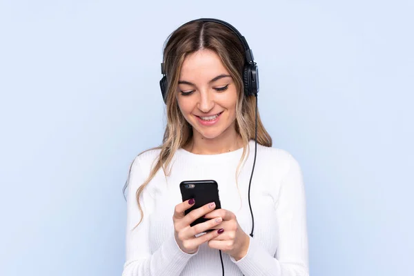 Mujer Joven Sobre Fondo Azul Aislado Escuchando Música Mirando Móvil — Foto de Stock