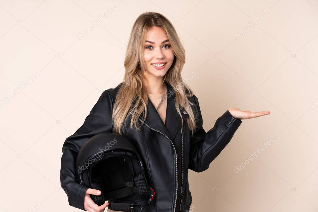 Russian girl with a motorcycle helmet isolated on beige background holding copyspace with two hands