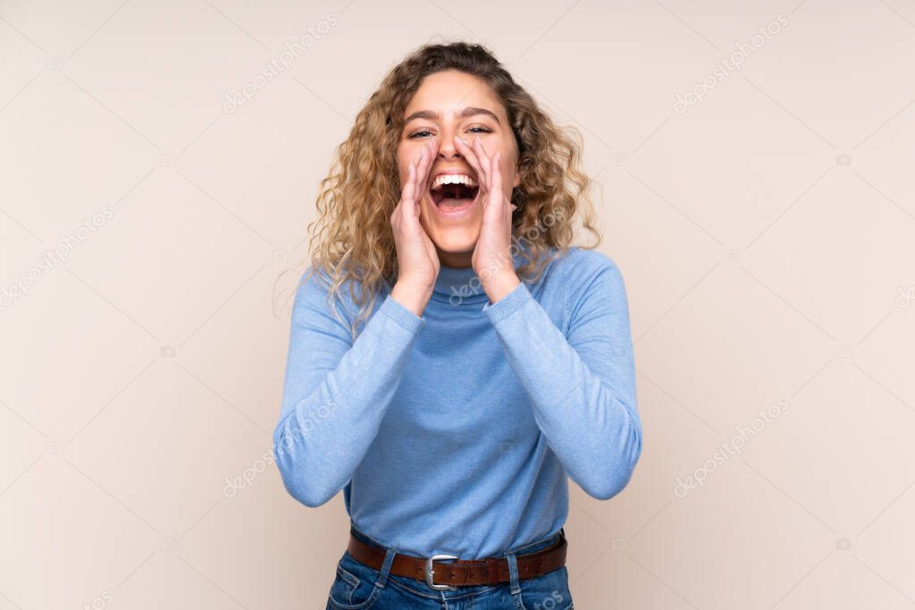 Young blonde woman with curly hair wearing a turtleneck sweater isolated on beige background shouting and announcing something