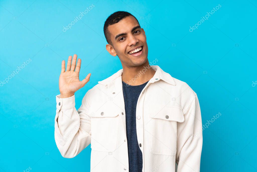 Young African American man over isolated blue background saluting with hand with happy expression