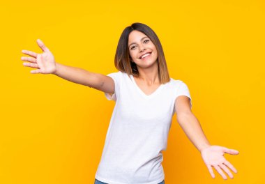 Izole sarı arka plan üzerinde genç kadın sunan ve el ile gelmek için davet