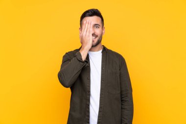 İzole edilmiş sarı arka planı olan bir adam bir gözü elle kapatıyor.