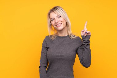 Izole sarı arka plan üzerinde genç sarışın kadın gösteren ve en iyi işareti bir parmak kaldırma