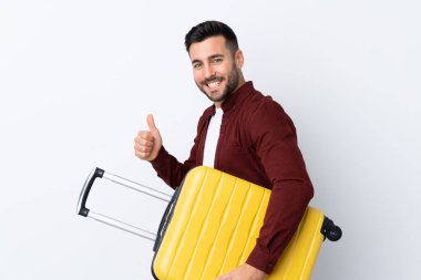 Genç yakışıklı adam izole edilmiş beyaz arka planda seyahat valiziyle ve başparmağıyla