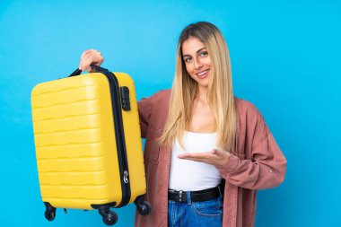 Genç Uruguaylı kadın izole edilmiş mavi arka planda seyahat valiziyle tatilde.