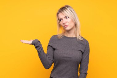 Sarışın genç kadın, izole edilmiş sarı arka planda. Kopyalama alanını kuşkulu tutuyor.