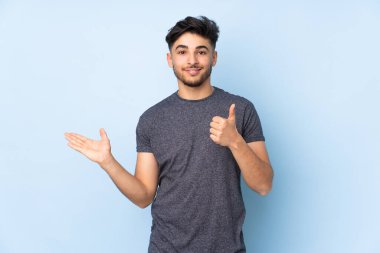 İzole edilmiş arka plan üzerinde yakışıklı Arap bir adam. Avucunun içinde hayali bir şey tutuyor. Bir ilan vermek için.