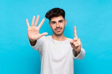 İzole edilmiş mavi arka plan üzerinde genç adam parmaklarıyla altı sayıyor.