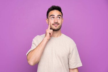 Soyutlanmış mor arka planda genç yakışıklı bir adam yukarı bakarken bir fikir düşünüyor.