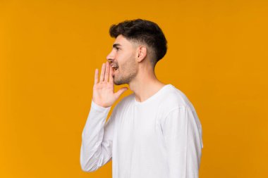 İzole edilmiş turuncu arka planda genç bir adam ağzı sonuna kadar açık bağırıyor.