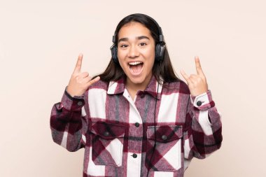 Genç Hintli kadın bej arka planda izole edilmiş rock hareketleri yapan müzik dinliyor.